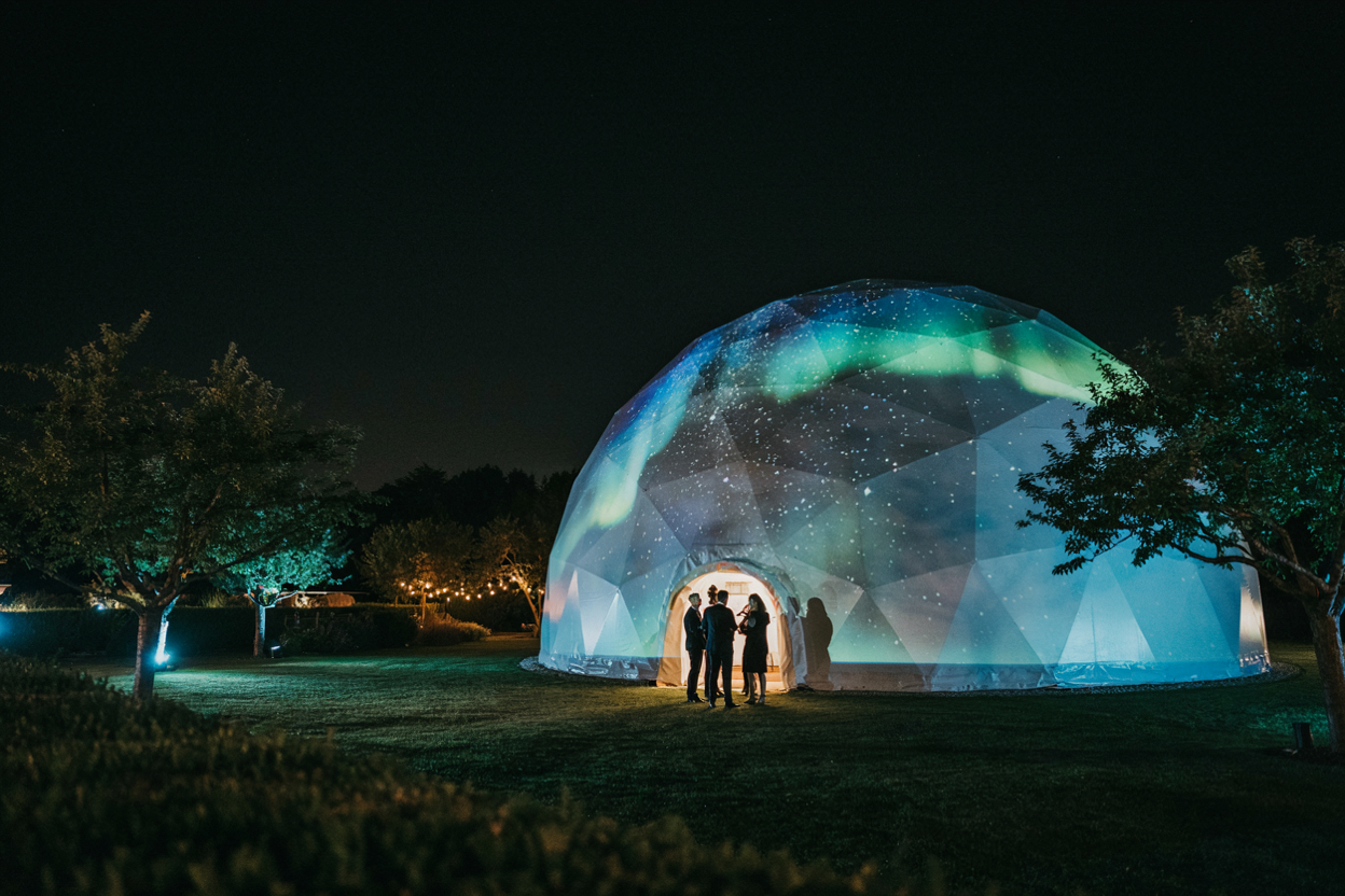 Dôme immersif illuminé la nuit avec projection d'aurores boréales lors d'un événement en extérieur